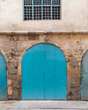 Closed turquoise weathered wooden arched door and wood window grill in stone bricks wall, located in old abandoned district
