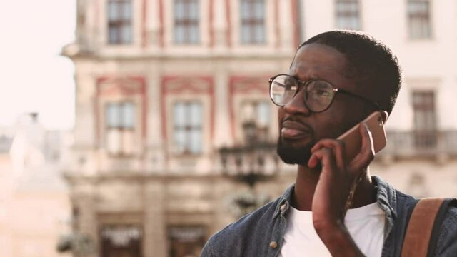 Young African American man talking on phone nodding his head. A smiling man standind in city center in sunlight.