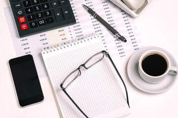 Office Desk with a calculator, Notepad, glasses, mobile phone, coffee Cup and financial papers. Business concept. Data analysis and marketing research