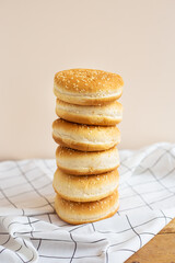 Freshly baked magnificent buns for hamburgers lie durg on each other in the form of a tower on a wooden table with a white checkered napkin. Close-up.