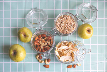 Delicious organic oatmeal with apples for breakfast. Raw oatmeal in a glass jar for cereals on a turquoise background. Nuts, dried apples, apple chips, freshly squeezed fruit juice.