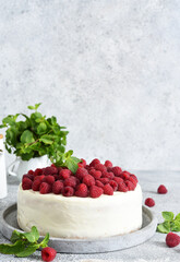 Birthday cake with cream and raspberries on a concrete kitchen background.