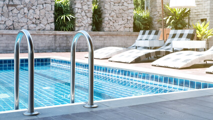 Closeup stair in the blue swimming pool with blurred sun-bed background