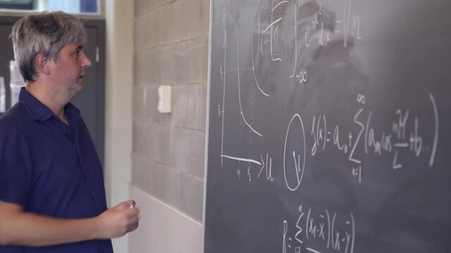 Middle Aged Math teacher writting formulas on a black board
