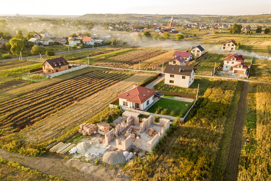 Top down aerial view of two private houses, one under construction with concrete foundament and brick walls and another finished with red tiled roof.