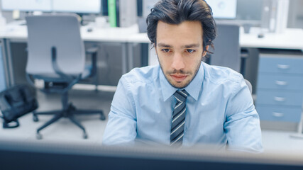 Handsome Motivated Office Worker Uses Desktop Computer, Typing on a Keyboard. Confidentand Young Businessman Works in the Big Bright Office with Team of Professionals