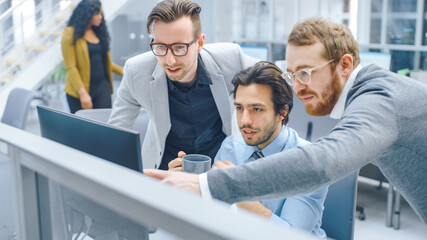 In Bright Modern Office: Businessman Sitting and Working at His Desktop Computer, Project Manager and Team Leader Standing Beside Him. They Have Discussion, Find Problem Solution, Pointing at Screen