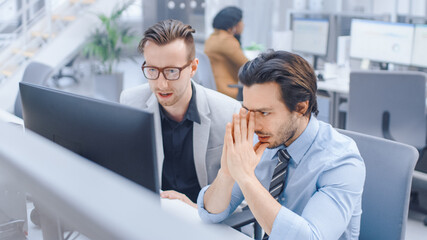 In Bright Modern Office: Handsome Office Worker Sitting and Working at His Desktop Computer, Discusses Problem Solution with His Male Project Manager. Diverse Team of Businesspeople Solving Problems