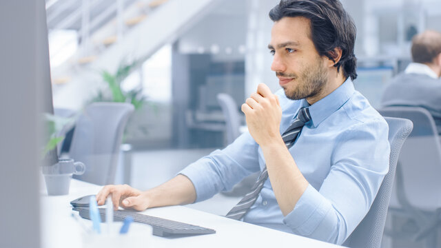 Portrait of Handsome and Confident Shirt and Tie Wearing Businessman Uses Desktop Computer, Typing on a Keyboard, Monitoring Business Transactions, Signing Contracts. Works in the Big Bright Office