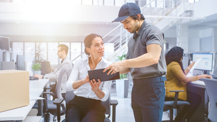 Delivery Man in Corporate Office, Hands Package to a Businesswoman, She signs Her Signature on the Tablet Computer. Modern Business Company Office. Shot with Warm Sun Flare Filter.