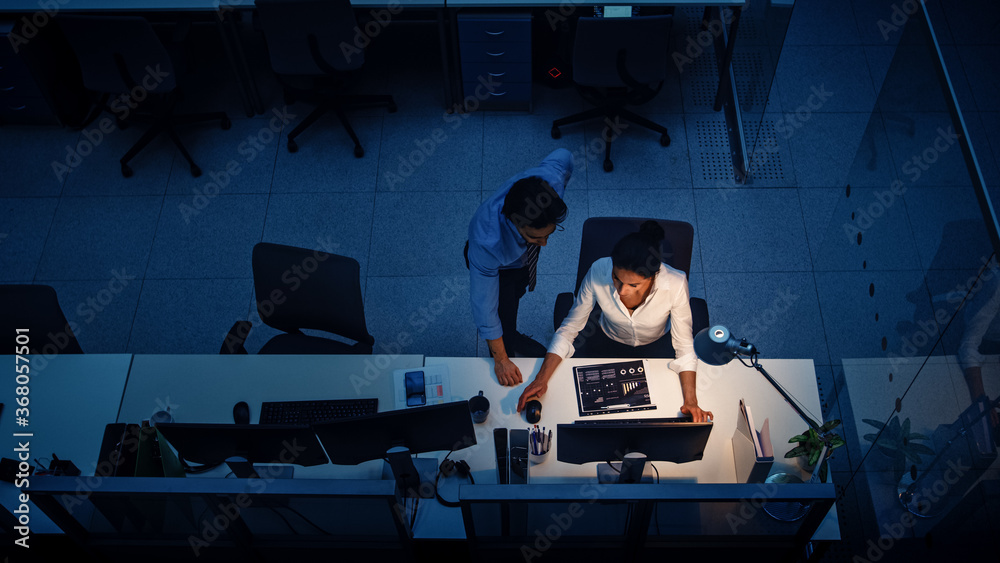Poster working late at night in the office: businesswoman and businessman using desktop computer, having di