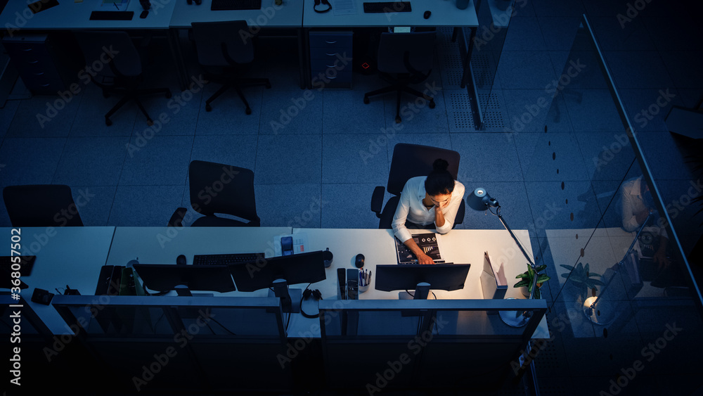 Poster working late at night in the office: businesswoman using desktop computer, analyzing, using document