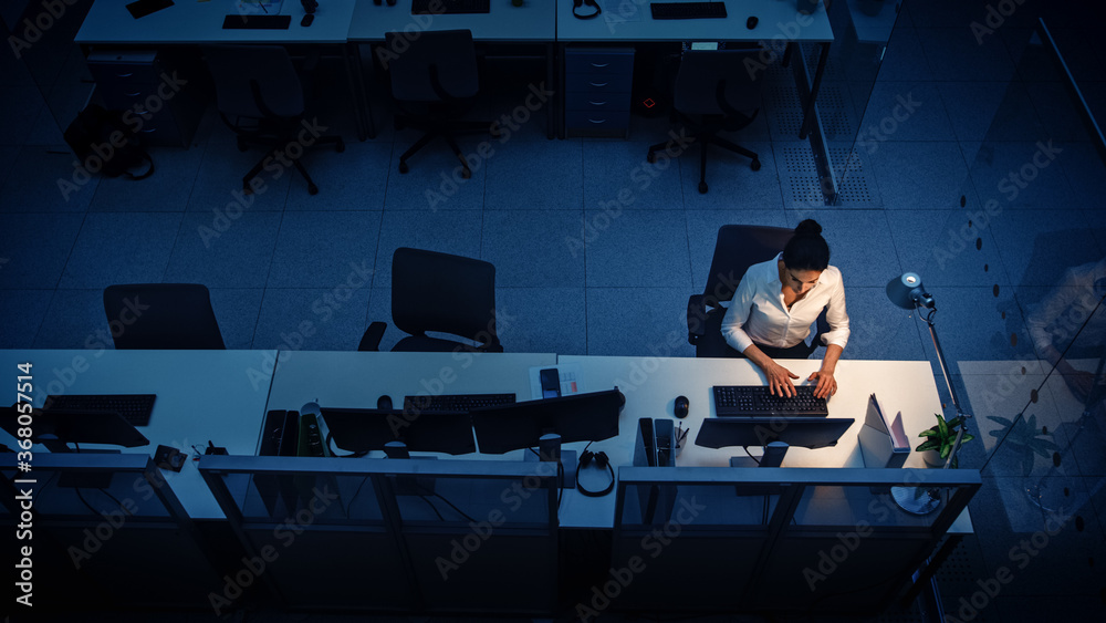 Poster alone working late at night in the office: businesswoman using desktop computer, analyzing, using do