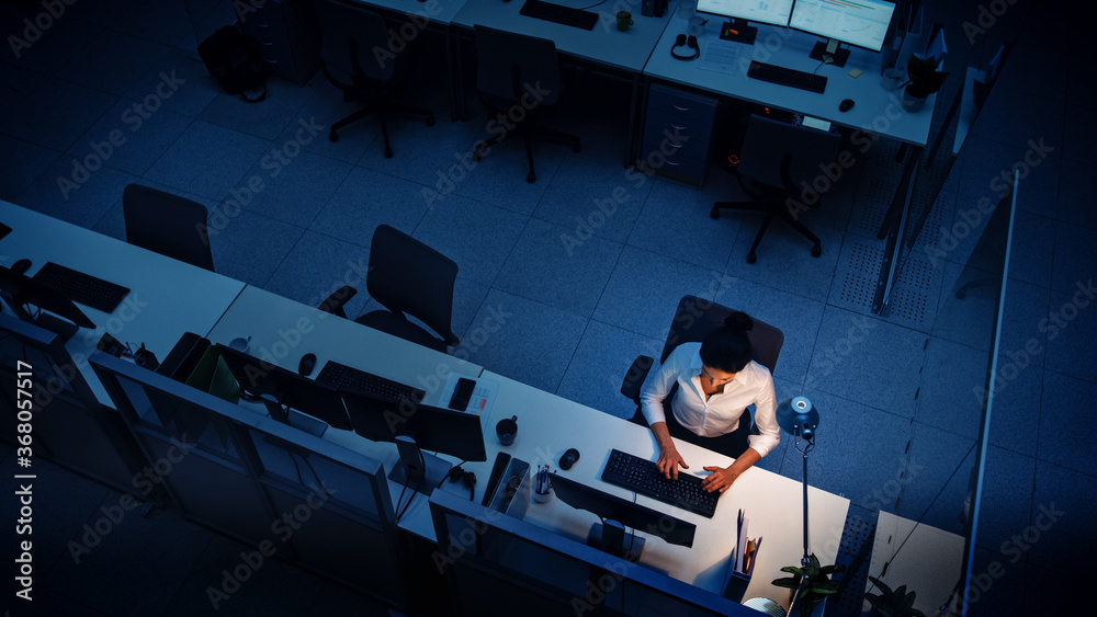 Poster alone working late at night in the office: businesswoman using desktop computer, analyzing, using do