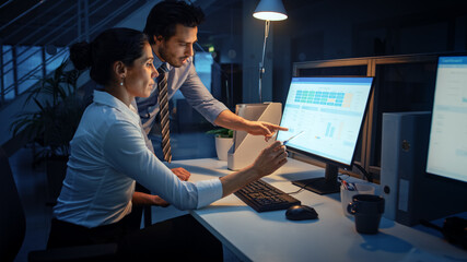 Late at Night In Modern Office: Businessman and Businesswoman Work on Desktop Computer, Having...