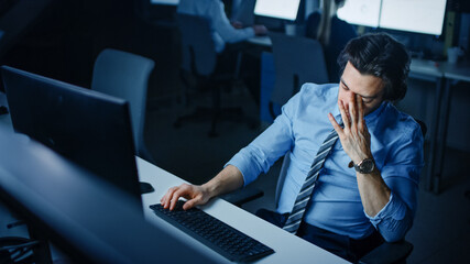 In the Office at Night Overworked Tired Office Worker Uses Desktop Computer Yawning. Tired Exhausted Businessman Finishing Important Project