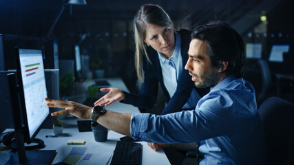 Confident Businessman Uses Desktop Computer, His Female Manager Explains Specific Tasks, Account Handling and Strategy. Professional People Discussion and Arguing Late at Night in Corporate Office.
