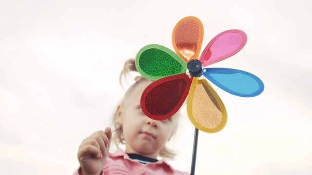 little daughter girl play pinwheel lifestyle a wind toy. happy family concept. child plays with windmill. portrait girl blonde kid holds flower toy spinning pinwheel. happy childhood