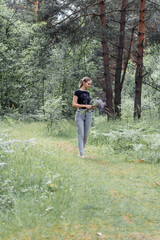 Obraz premium young woman with a tail of hair in a black t-shirt and gray jeans in the woods holding blue wildflowers in her hands