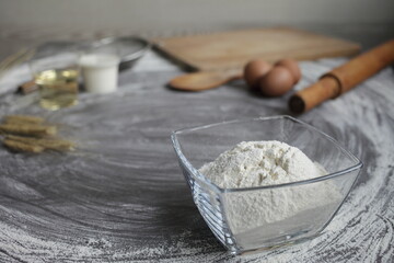 Flour, egg, olive oil, milk, wheat ears, kitchen tool on gray table background.