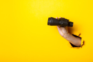 Woman's hand holds black binoculars on a yellow background. Travel, find and search concept