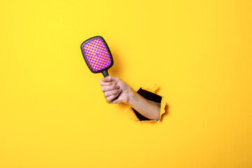 Female hand holds a large hairbrush on a yellow background. Hair accessories