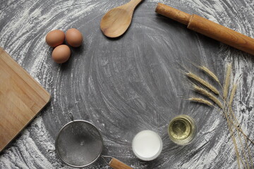 Egg, flour, olive oil, milk, wheat ears, kitchen tool on gray table background.