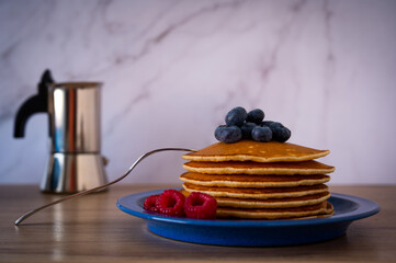 Pancakes with fresh berries a on the blue plate with espresso pot in background.