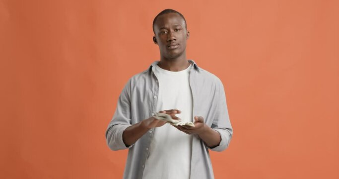 Serious black man throwing money, orange background