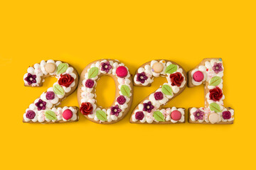 2021 cake decorated with flowers isolated on yellow background. New year concept.