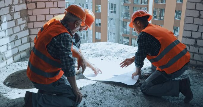 Three builders talking and working with blueprint on construction site