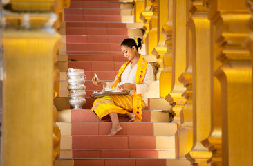 Portrait of a young Myanmar woman in a traditional welcoming dress and gesture with Shwedagon pagoda in the background.