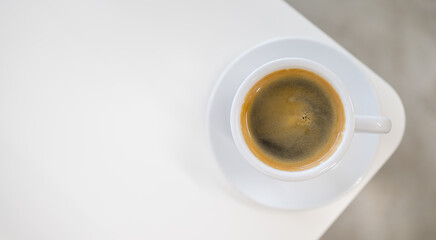 Top view of white cup of hot black coffee and crema on white table .
