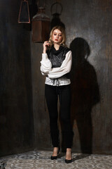 Fashion vogue style full length portrait of young gorgeous blonde female model in black trousers and white blouse standing against grunge metal wall
