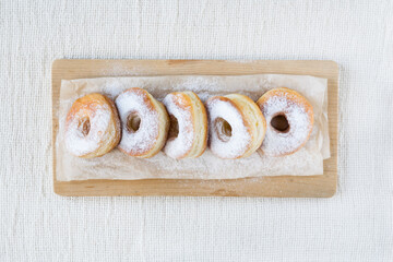 Row of sugar powdered donuts on a paper on light rustic textile background, horizontal orientation, selective focus