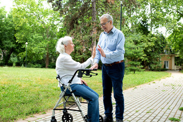 Senior woman sitting in her rolling walker being accompanied with a senior man