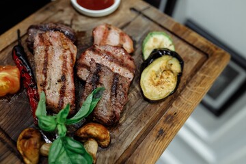 Three types of grilled meat with grilled vegetables on a wooden board. A waiter hand in a glove with a serving board on which grilled meat