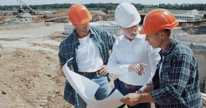 Engineer and builders talking and looking at blueprint on construction site