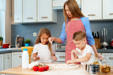 Young mother and her cute kids cooking pizza together