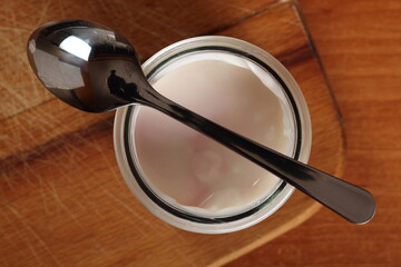 Yogurt in open small glass jar with spoon on wooden cutting board. DIrectly Above.