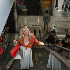Portrait of a beautiful woman with shopping bags in the mall on the escalator and looking to the side. Young shopaholic.