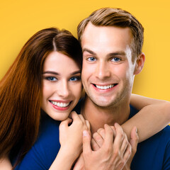 Smiling attractive young amorous couple. Portrait picture of embracing models at happy in love studio concept, isolated over orange yellow color background. Man and woman posing together. Square photo