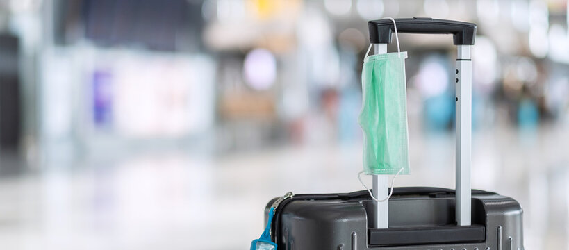 Luggage bag with surgical face mask and alcohol gel hand sanitizer in international airport terminal, protection Coronavirus disease (Covid-19) infection. New Normal and travel bubble concepts