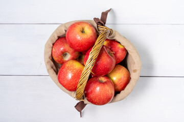 basket with ripe red social apples on white wooden background
