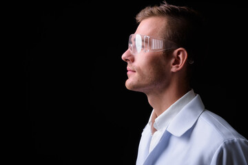 Portrait of young handsome man doctor as scientist with protective glasses