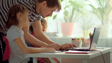 Cute children use laptop for education, online study, home studying, Boy and Girl have homework at distance learning. Lifestyle concept for home schooling. Father helps daughter and son.