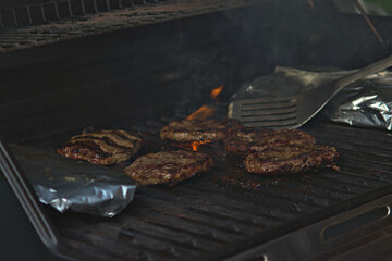 Hamburgers on Barbeque with potatoes wrapped in tinfoil.