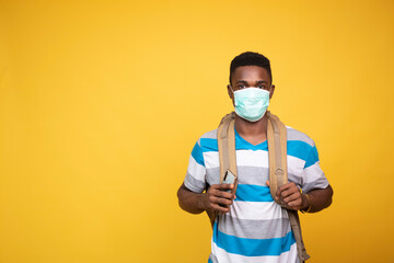 young black man carrying a backpack and wearing a face mask using his mobile phone
