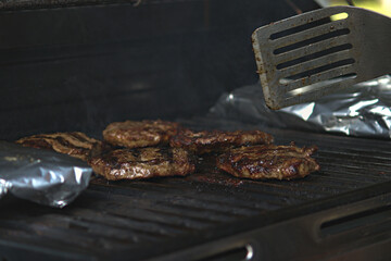 Hamburgers on Barbeque with potatoes wrapped in tinfoil.