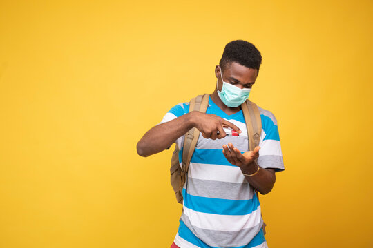 A Young Black Man Carrying A Backpack And Wearing A Face Mask Using Hand Sanitizer